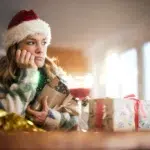 Mujer con gorro de Santa Claus con aspecto triste frente a una copa de vino y paquetes de Navidad