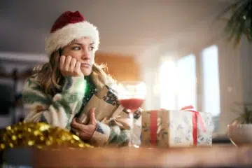 Mujer con gorro de Santa Claus con aspecto triste frente a una copa de vino y paquetes de Navidad